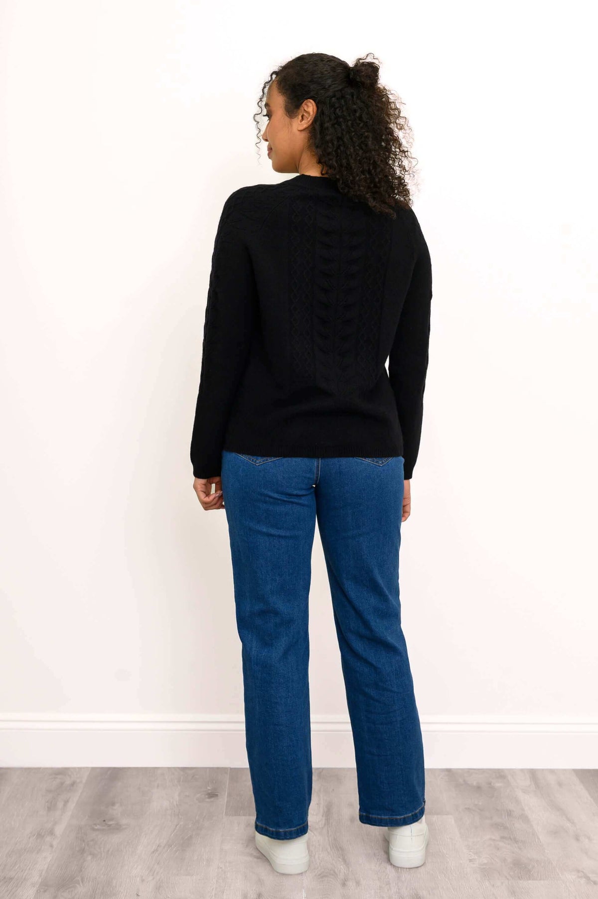 Back view of a woman wearing a black cable knit cardigan with detailed stitching