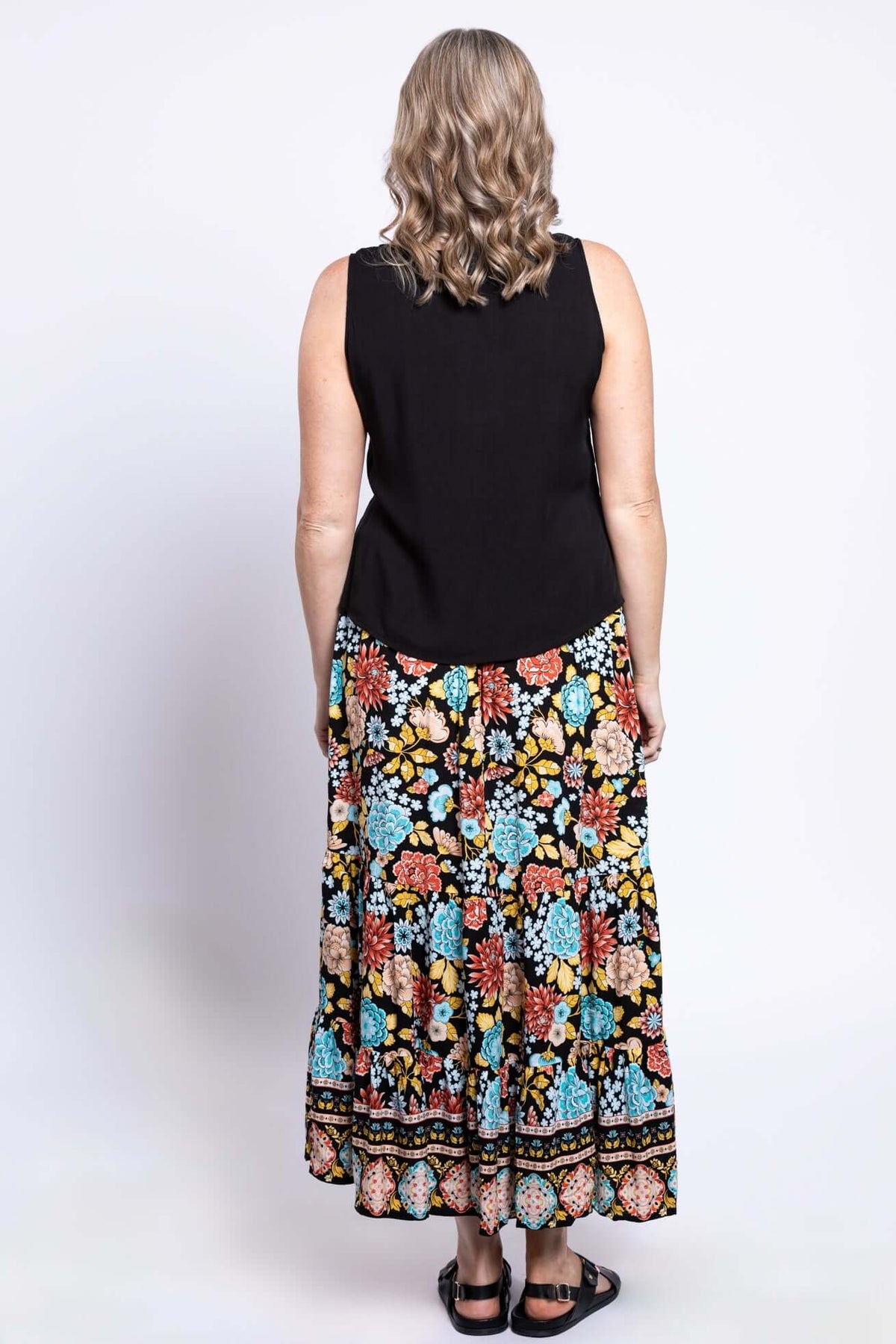 Back view of a woman wearing a black top and black floral maxi skirt with colorful pattern