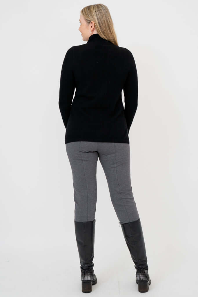 Back view of woman in black mock neck sweater and grey pants