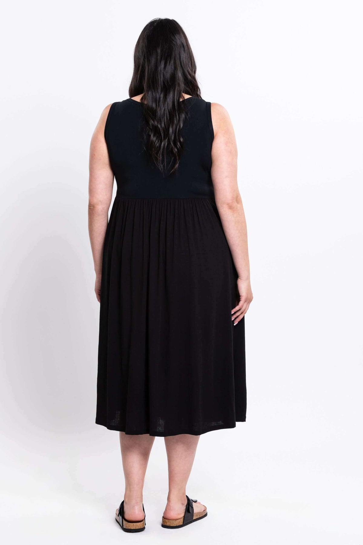 Back view of a woman wearing a black sleeveless midi dress with an empire waist