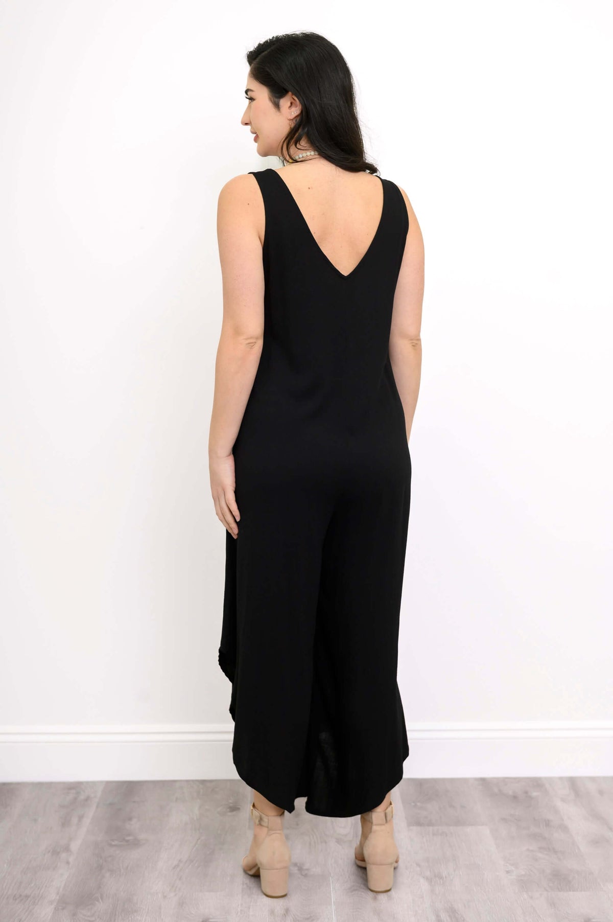 Back view of model showcasing V-back of black sleeveless jumpsuit
