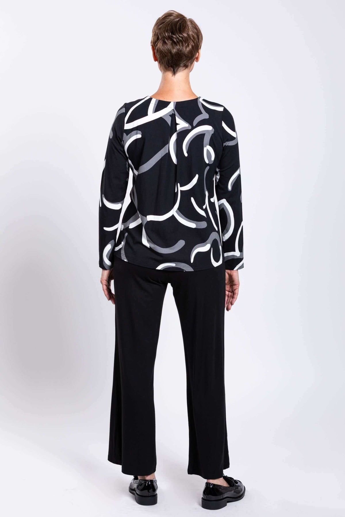 Back view of model wearing black long sleeve swirl print top and black pants