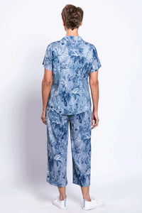 Back view of woman in blue botanical print shirt and cropped pants with white sneakers