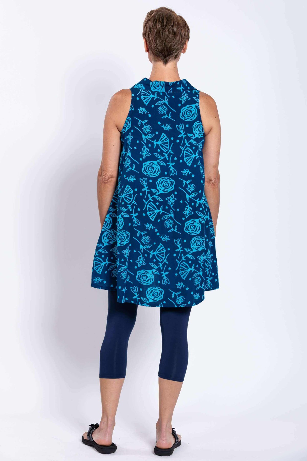 Back view of model wearing sleeveless blue A-line tank with bright floral print