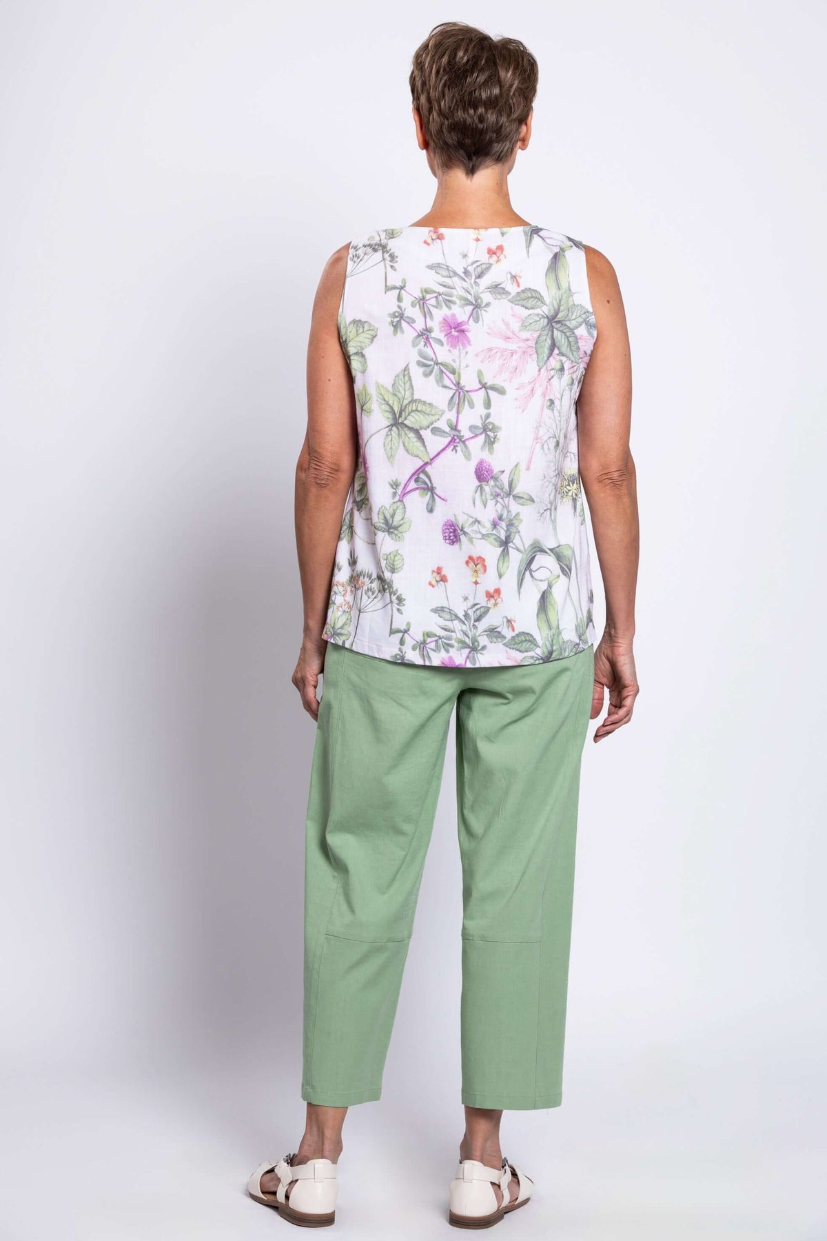 Back view of woman wearing botanical print tank top and green pants with white sandals