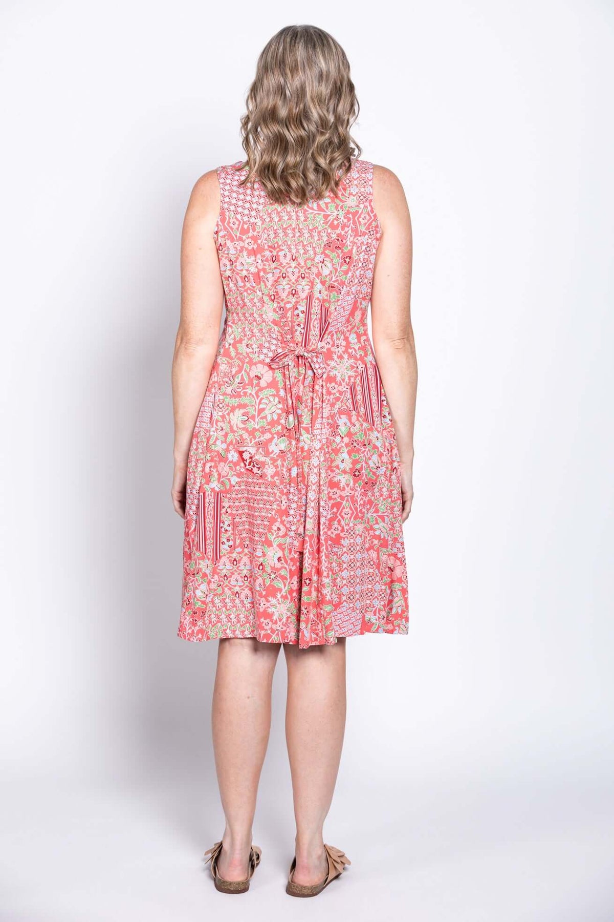 Back view of woman in coral floral sleeveless dress with tie-belt detail