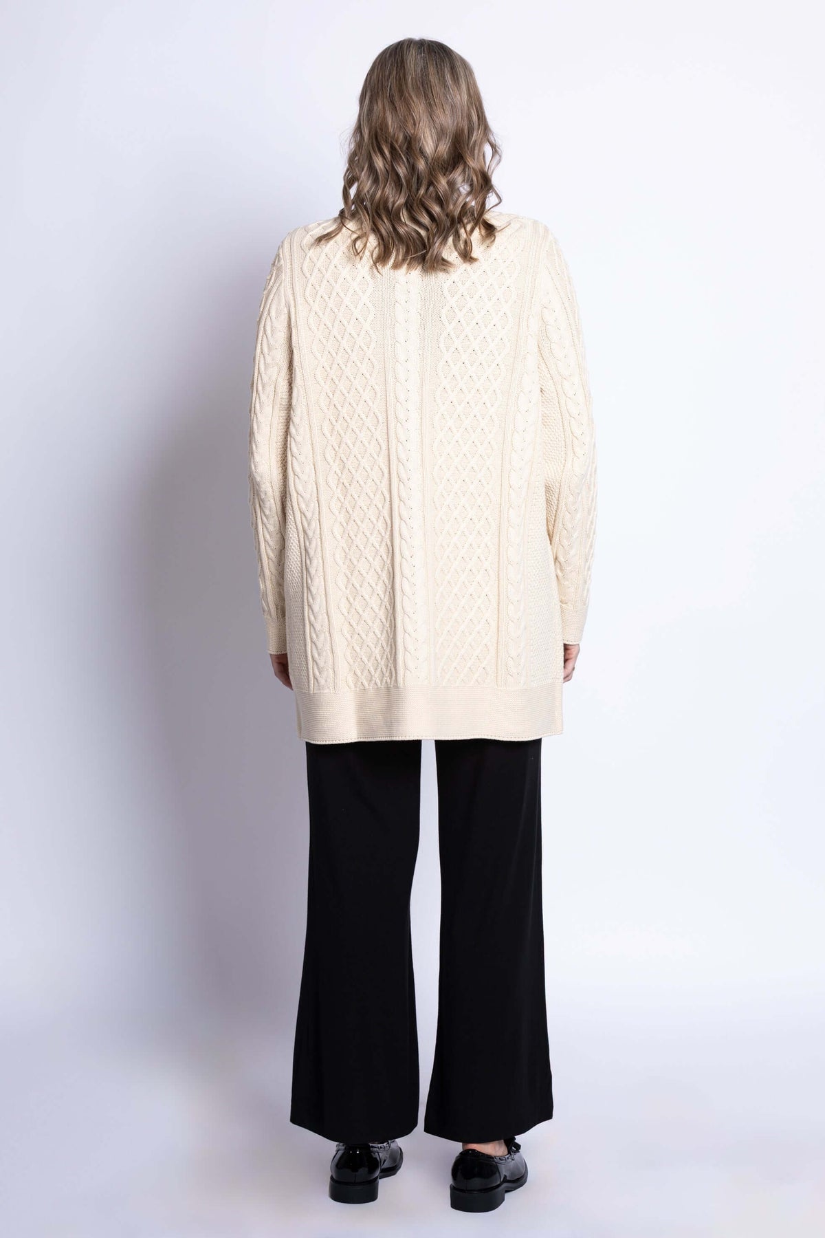 Back view of woman wearing a cream cable knit cardigan displaying the textured knit pattern