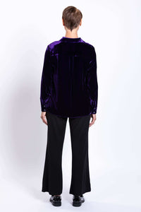 Back view of a woman wearing a deep purple velvet blouse and black pants