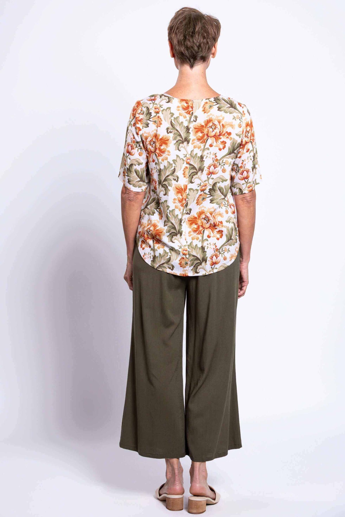 Back view of woman in floral blouse and olive wide-leg pants, sandals visible