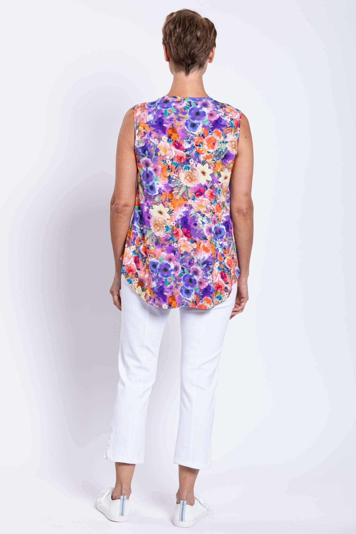 Back view of a woman wearing a floral sleeveless V-neck top with white pants