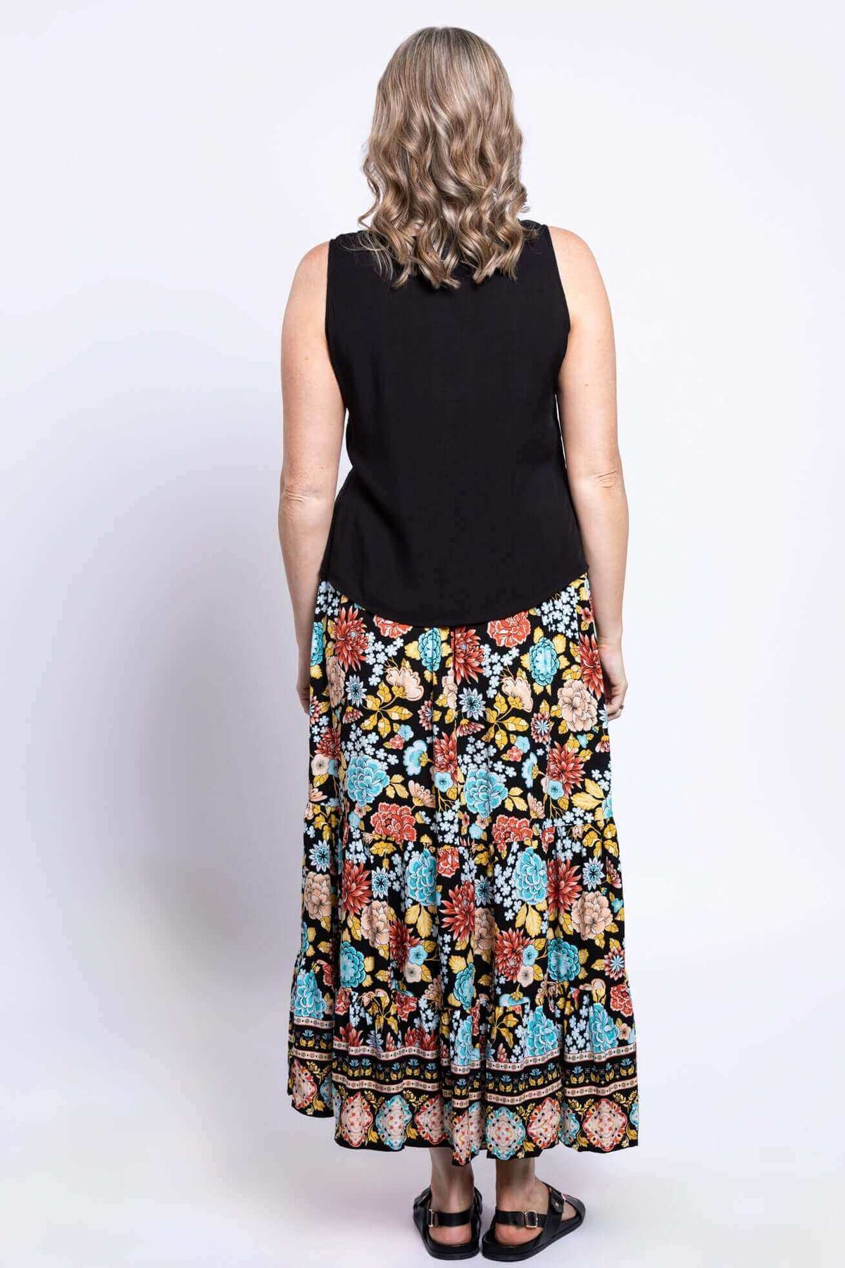 Back view of a woman wearing a sleeveless black top and floral tiered maxi skirt