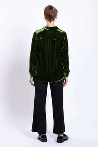 Back view of woman wearing a green silk velvet blouse and black pants