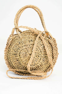 Back view of hand woven rattan bag displaying long braided strap and circular shape