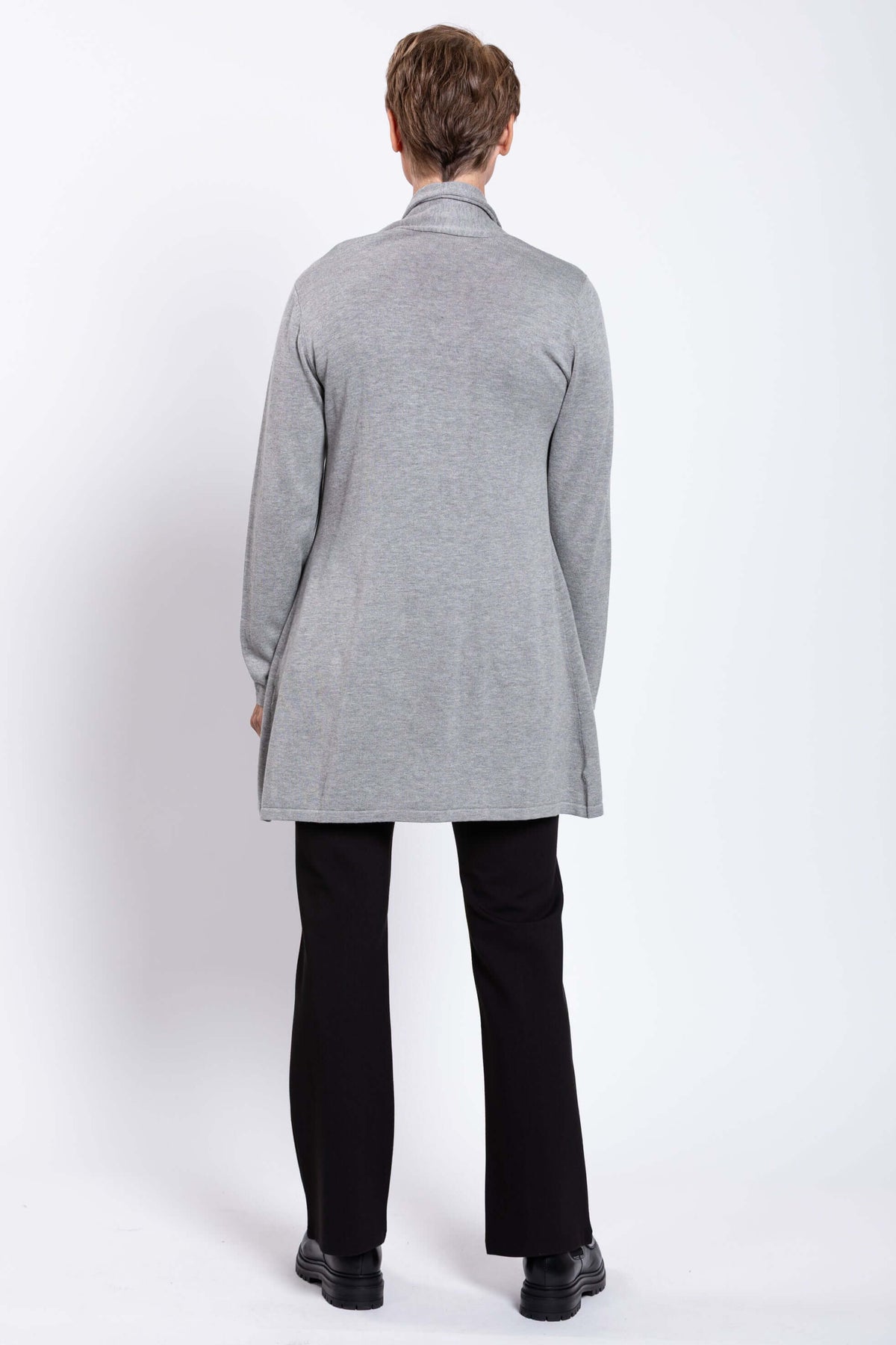Back view of a woman in a long grey cardigan sweater, black pants and boots