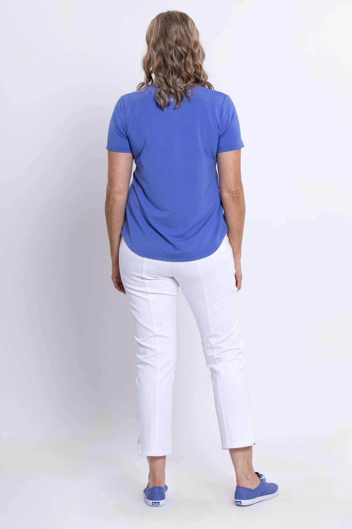 Back view of woman in blue scoop neck tee and white pants, showing curved hem