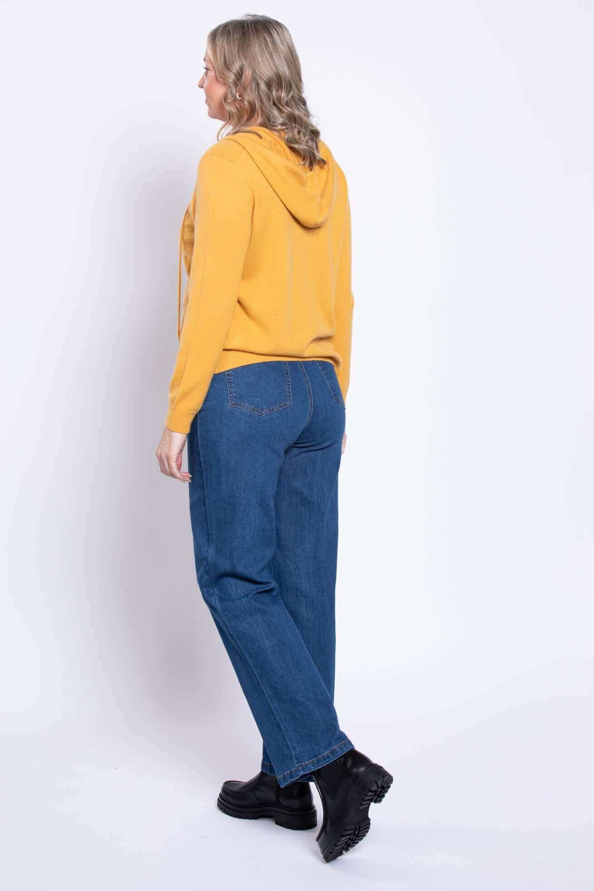 Back view of a woman in blue straight leg jeans with a yellow hoodie and black boots.