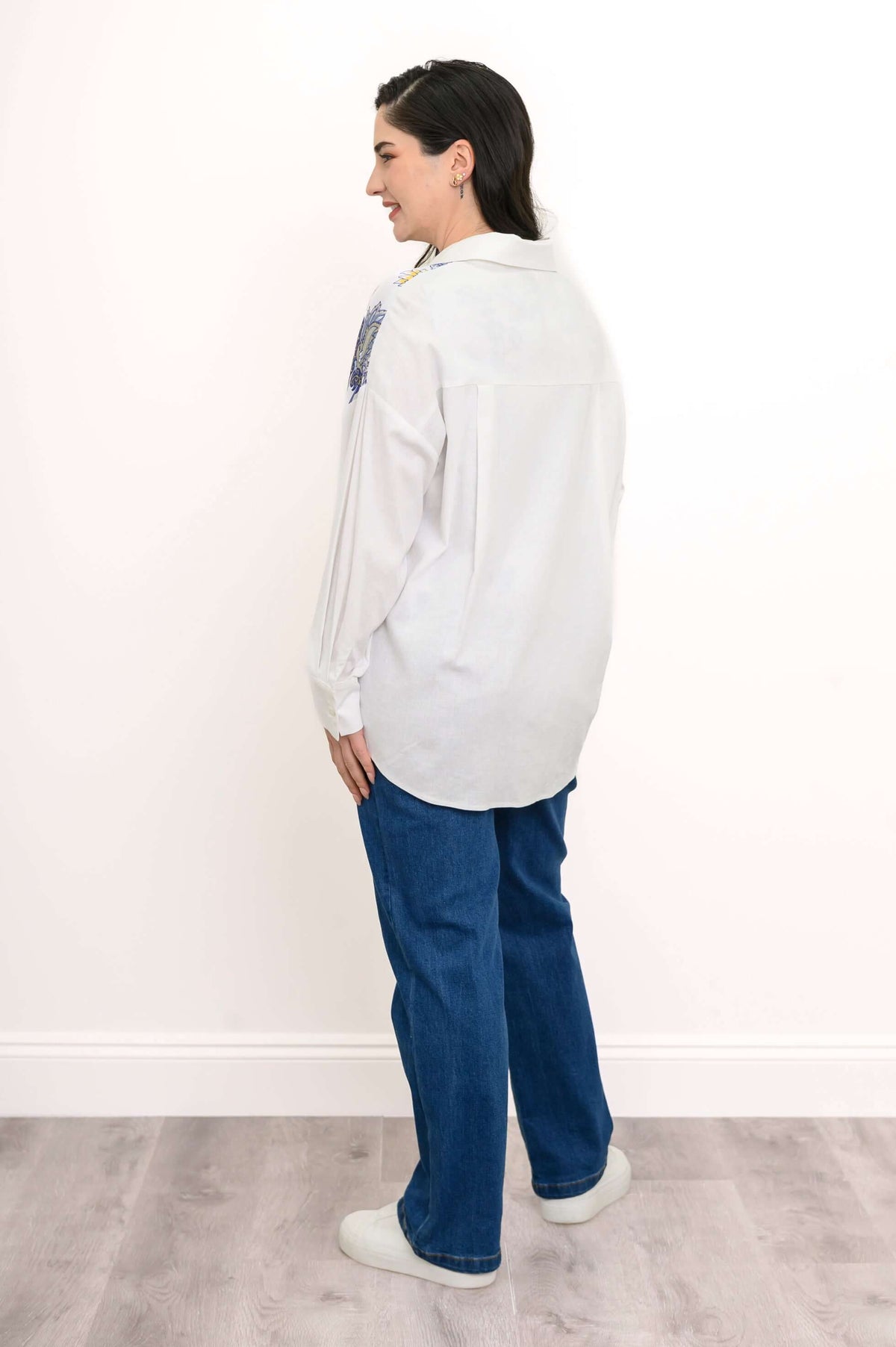 Back view of model in white blouse with printed yoke and blue jeans