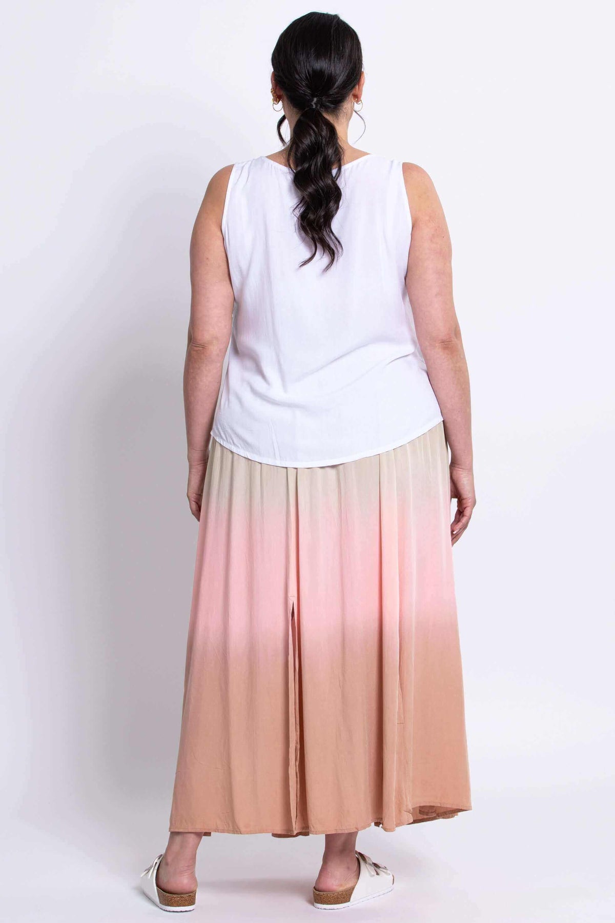 Back view of model in white sleeveless blouse and flowing dip-dye peach pink skirt