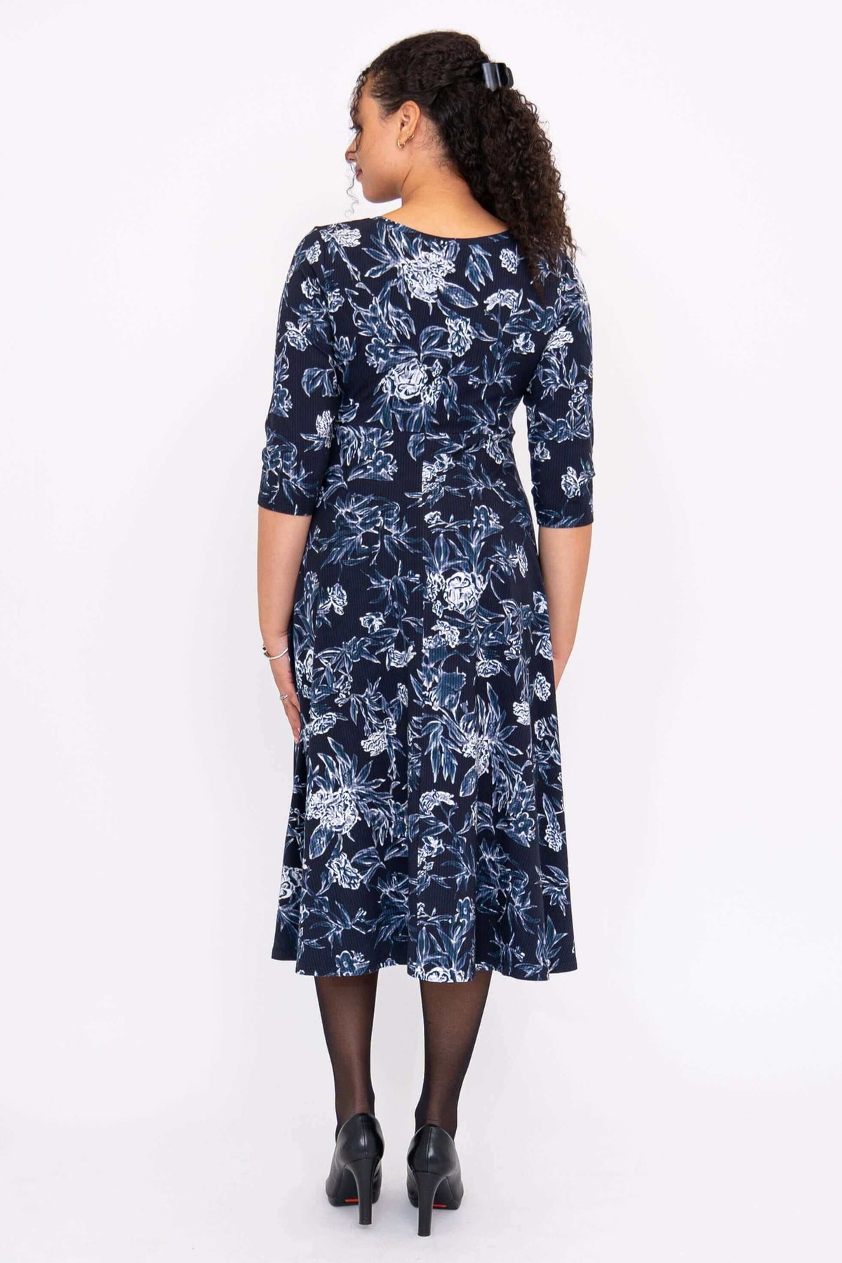 Back view of woman modeling navy floral midi dress with gentle A-line skirt
