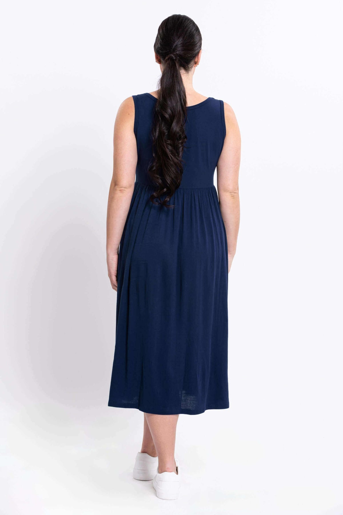 Back view of woman wearing sleeveless navy empire waist midi dress and white sneakers