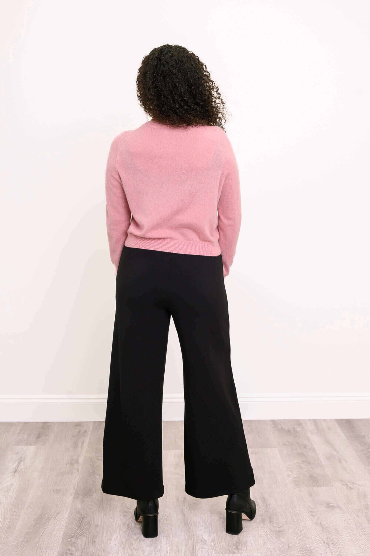 Back view of pink cashmere cardigan worn with black wide-leg pants