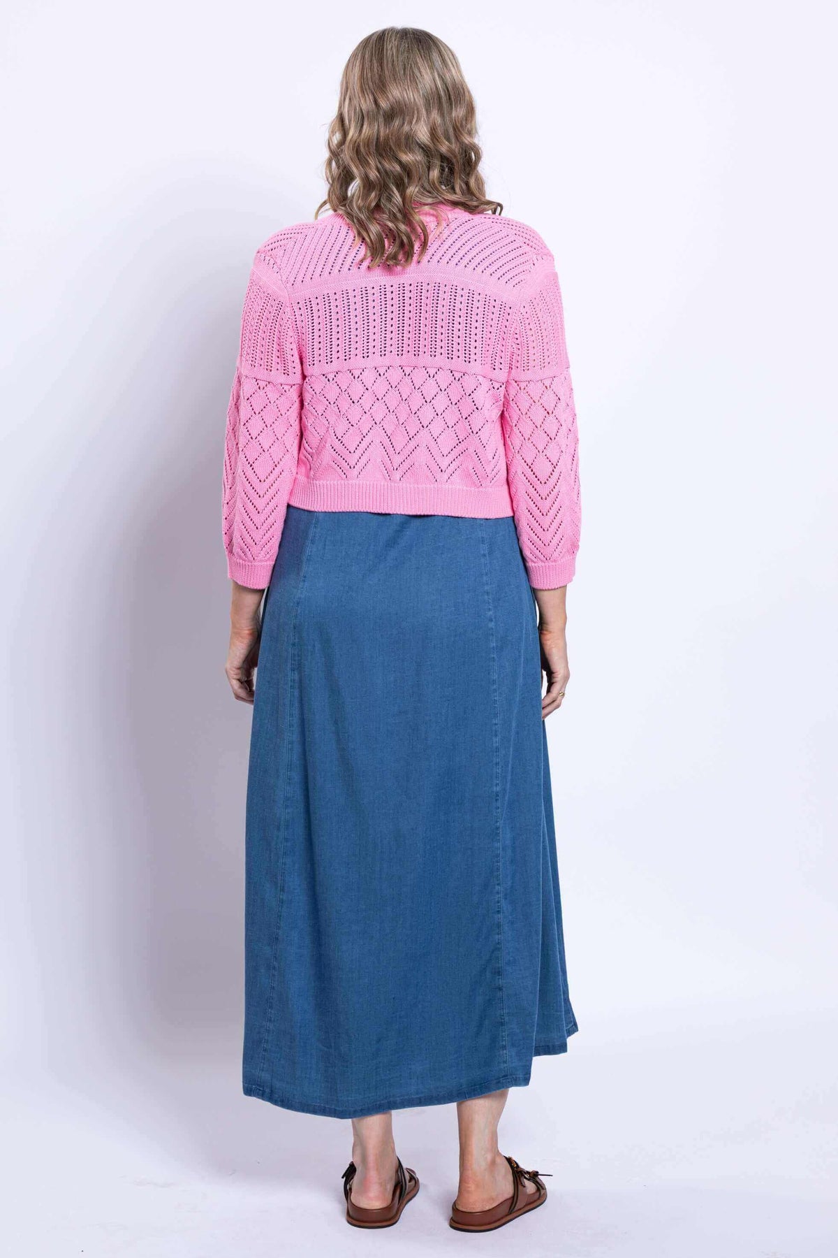Back view of woman wearing pink pointelle knit cardigan and blue dress