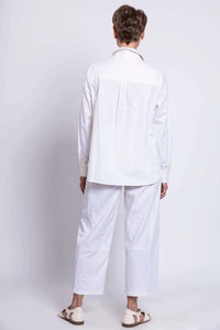 Back view of a woman wearing a relaxed white button-up shirt and white pants