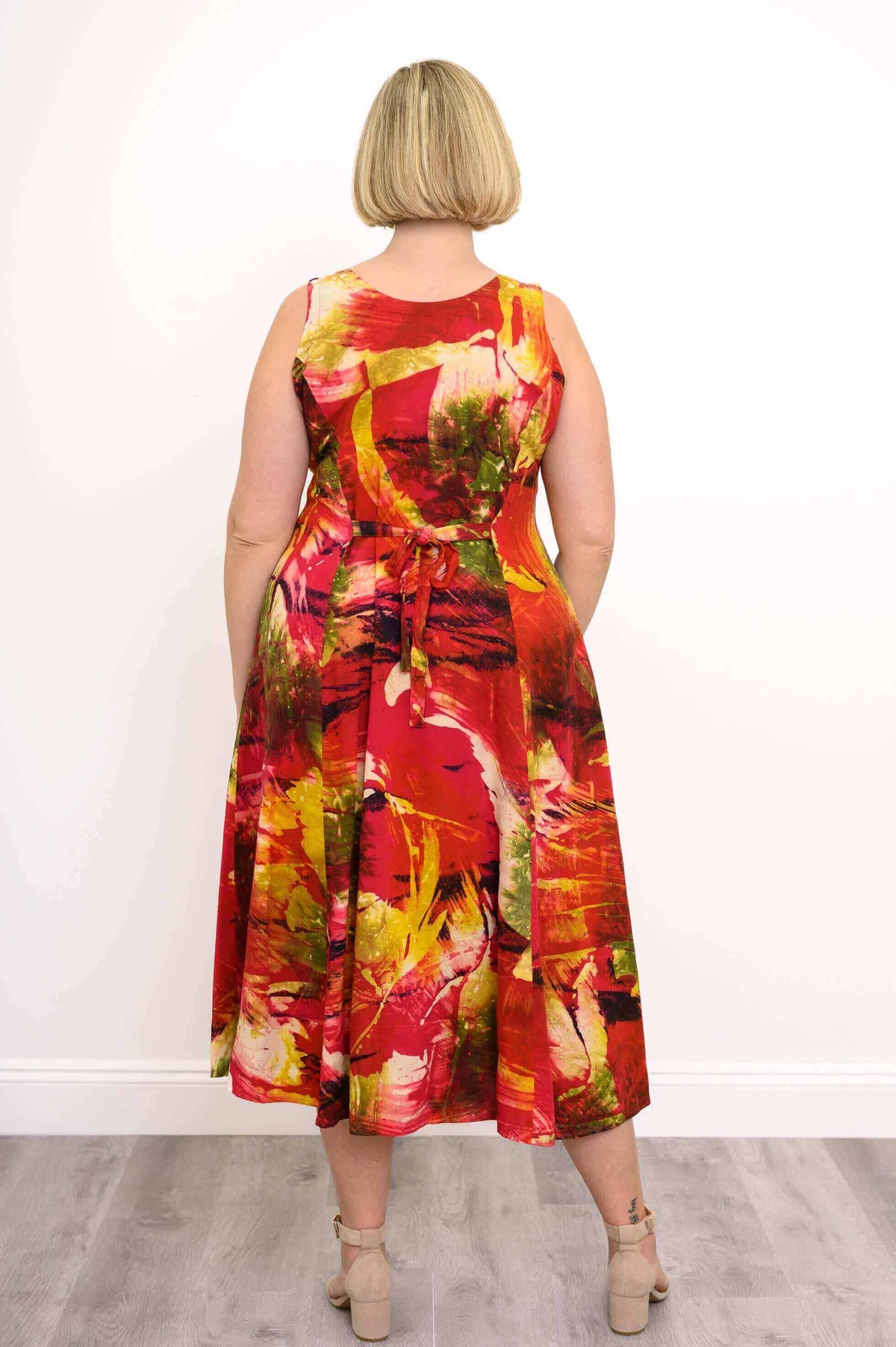 Back view of woman wearing sleeveless midi dress with tie-back waist and colorful abstract print