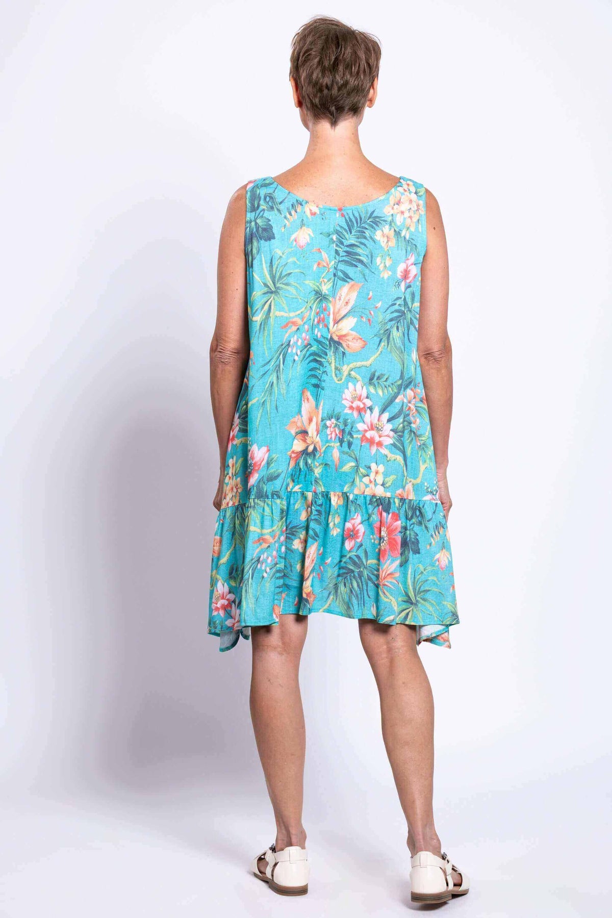 Back view of woman wearing turquoise dress with tropical floral print and ruffle detail