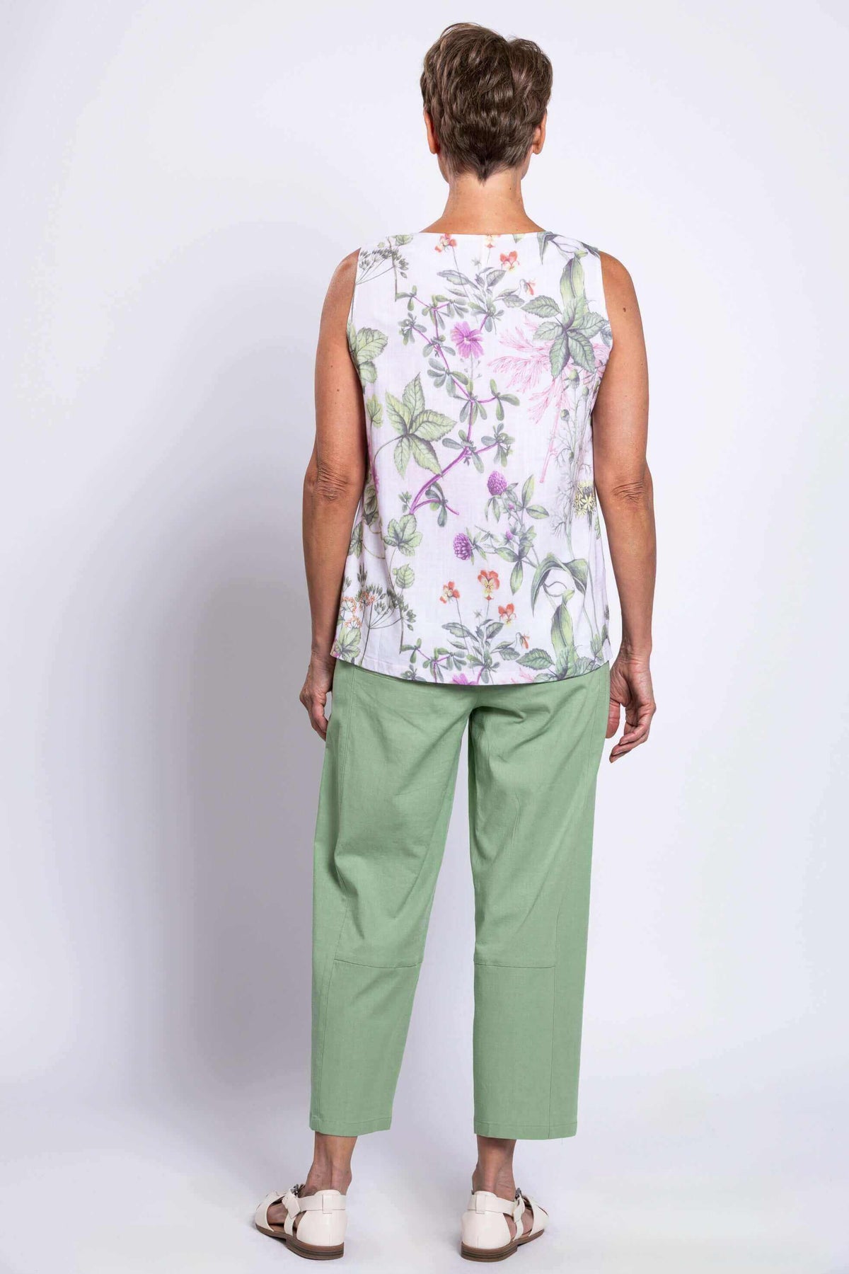 Mature woman modeling the back of a white botanical print tank top and green pants