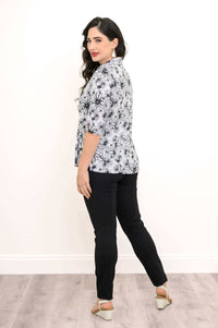 Back view of woman in a white floral blouse and black pants with white sandals