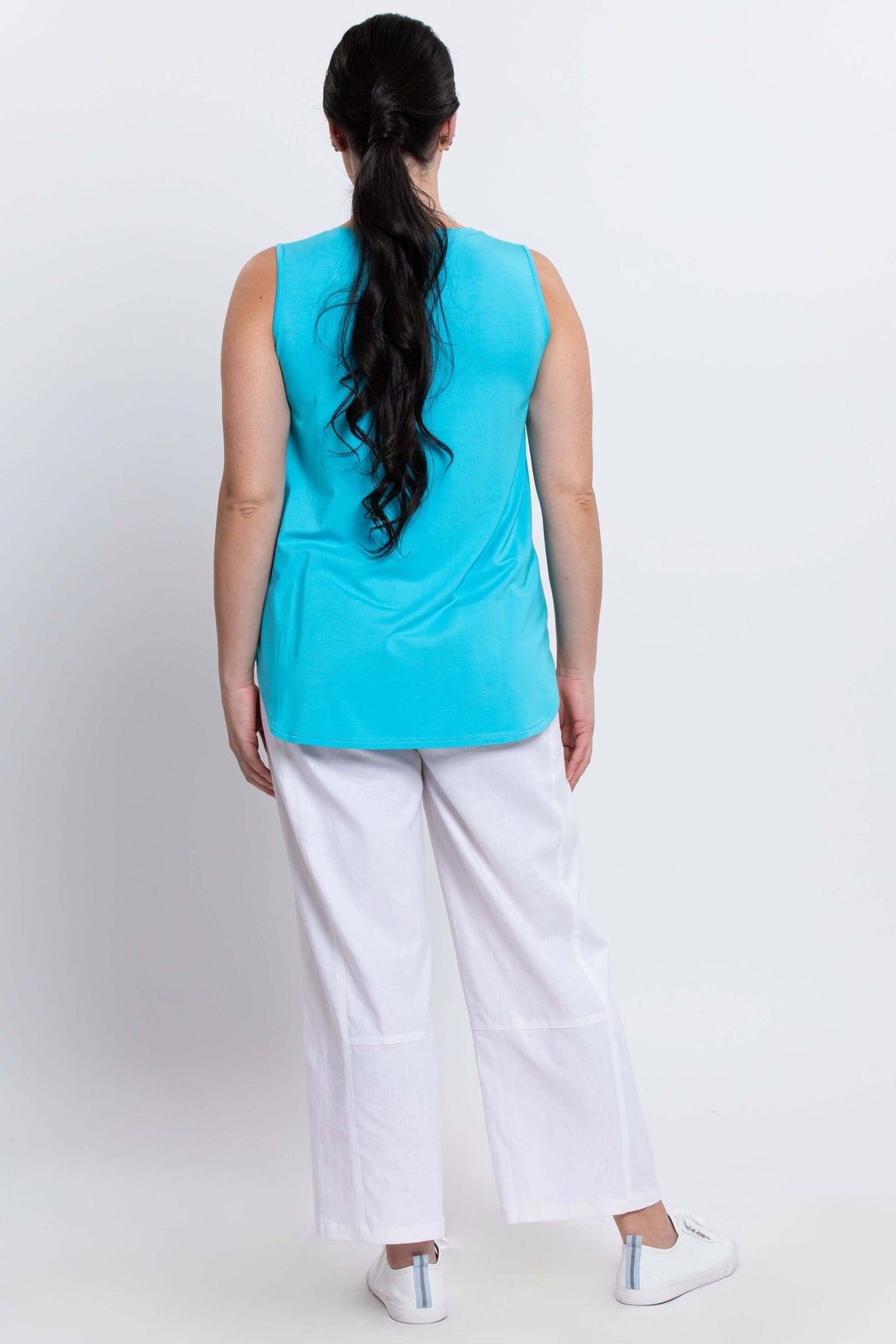 Back view of woman in aqua blue sleeveless tank top and white pants