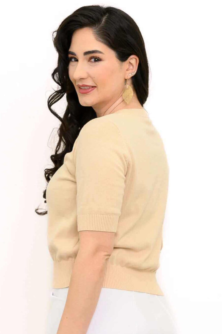 Back and side view of a woman in a beige short sleeve cardigan and white pants