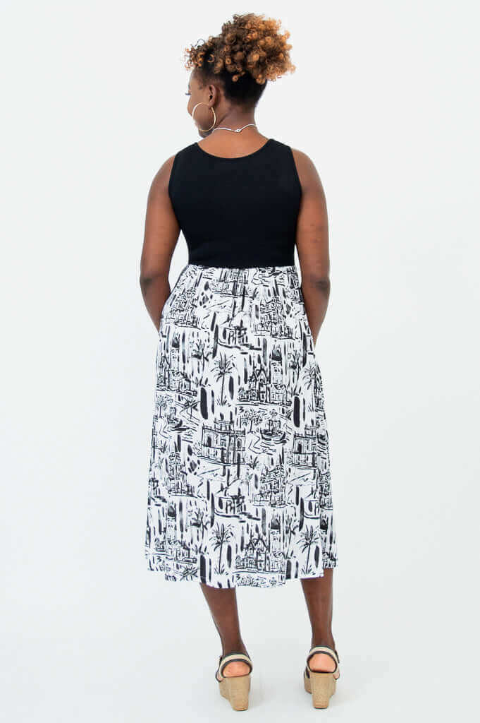 Back view of a woman in a sleeveless black and white midi dress with cityscape print
