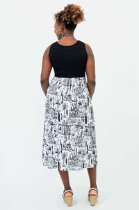 Back view of a woman in a sleeveless black and white midi dress with cityscape print