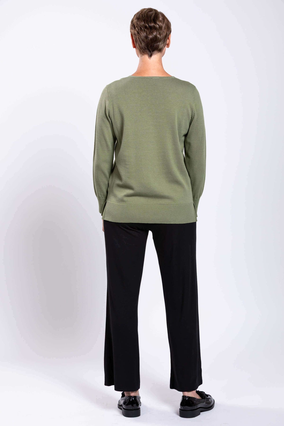 Rear view of woman in green V-neck sweater and black pants, showing back details
