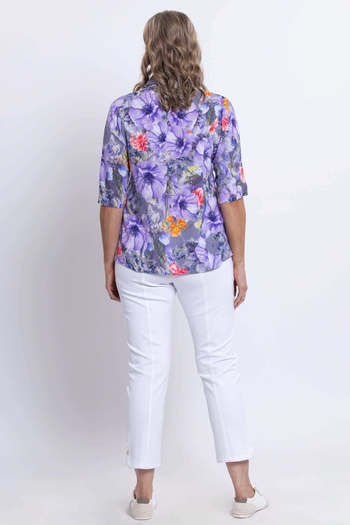 Back view of woman in purple floral blouse with elbow-length sleeves and white pants