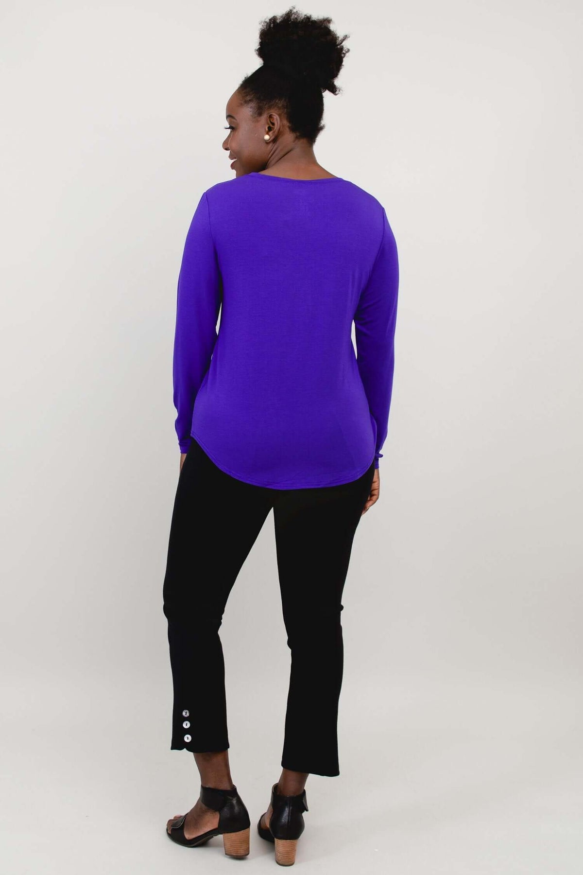 Back view of woman in a purple long sleeve shirt with rounded hem and black pants