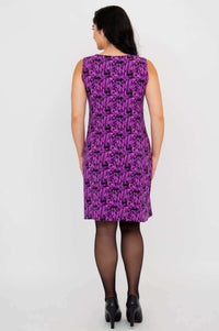 Back view of woman wearing a purple patterned shift dress and black heels
