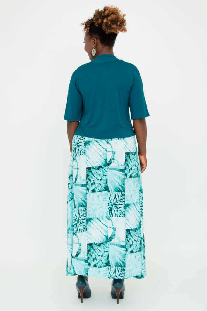 Back view of woman in teal cropped Doda Jacket and long green patterned dress