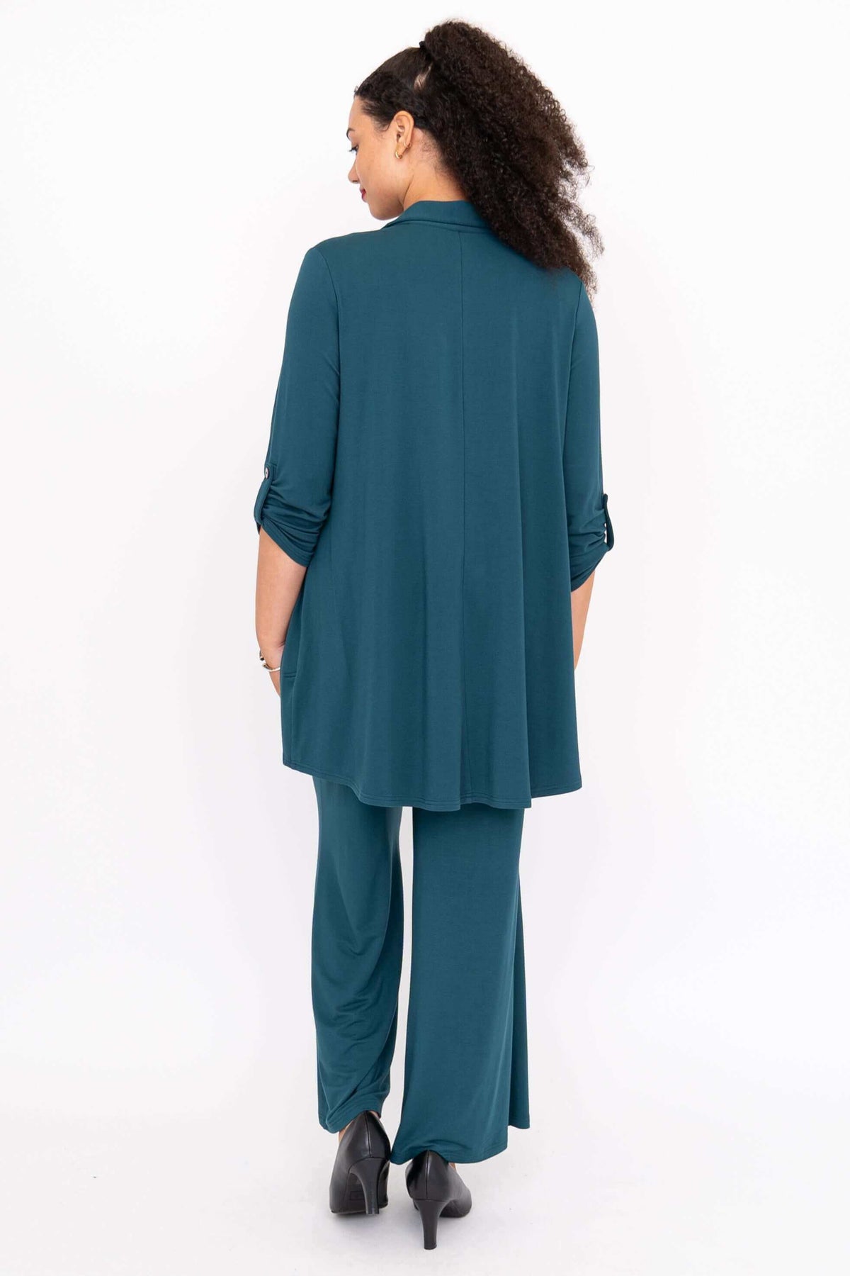 Back view of woman in teal wide leg pants and matching shirt, looking to the side, relaxed pose