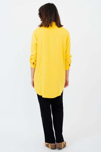 Back view of woman wearing yellow long-sleeve shirt tunic with black pants