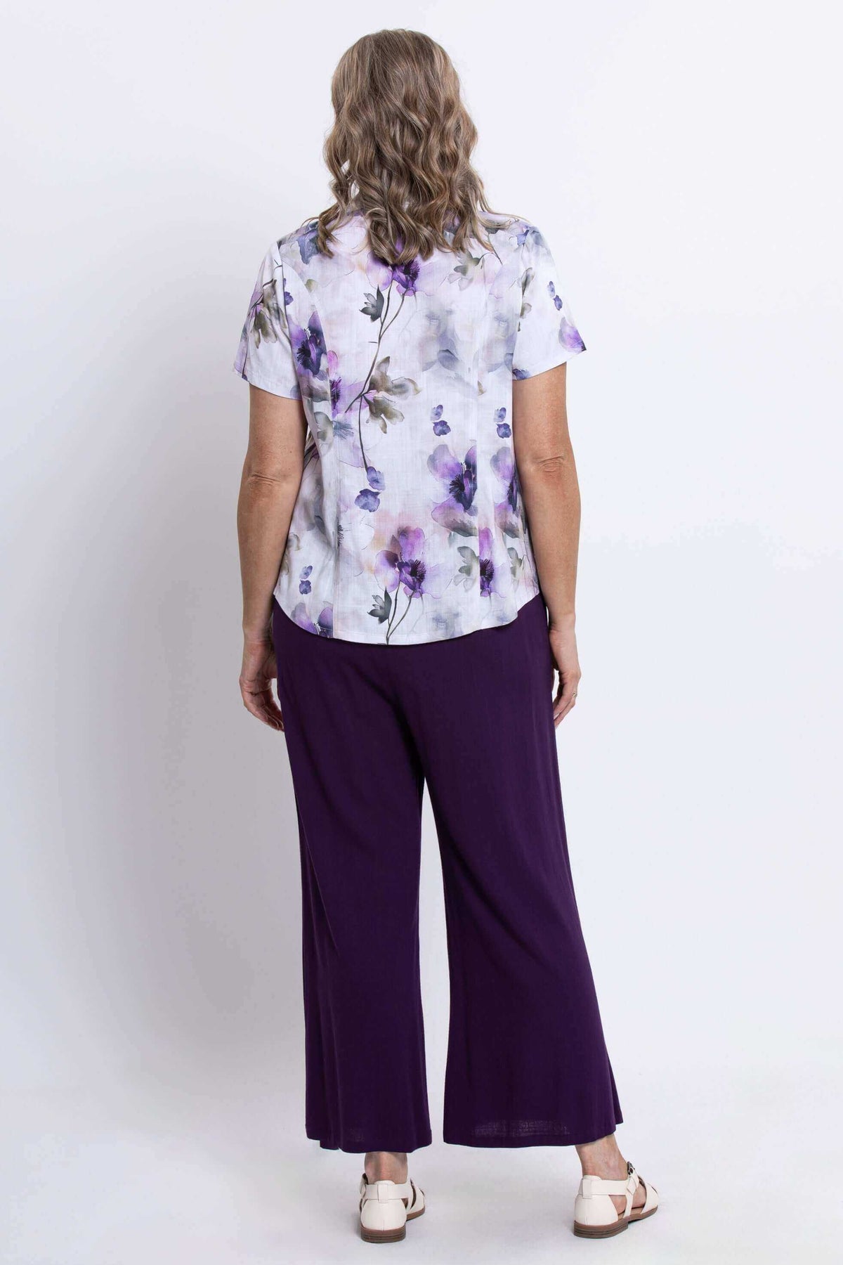 Back view of woman wearing a floral bamboo-linen blouse with purple wide-leg pants