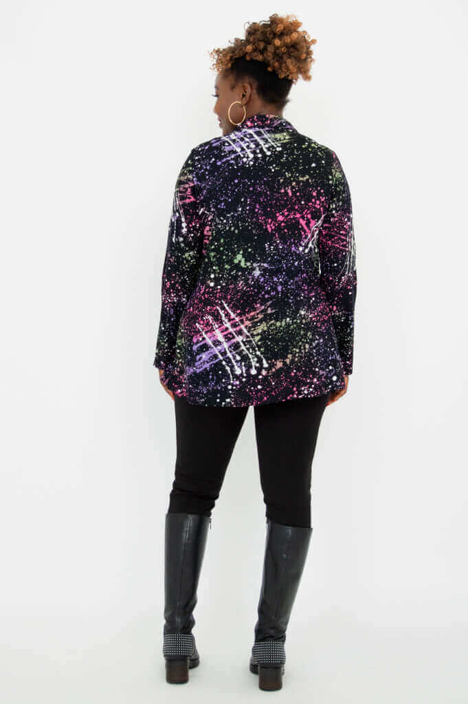 Back view showing the vibrant abstract print tunic with long sleeves, black pants, and boots