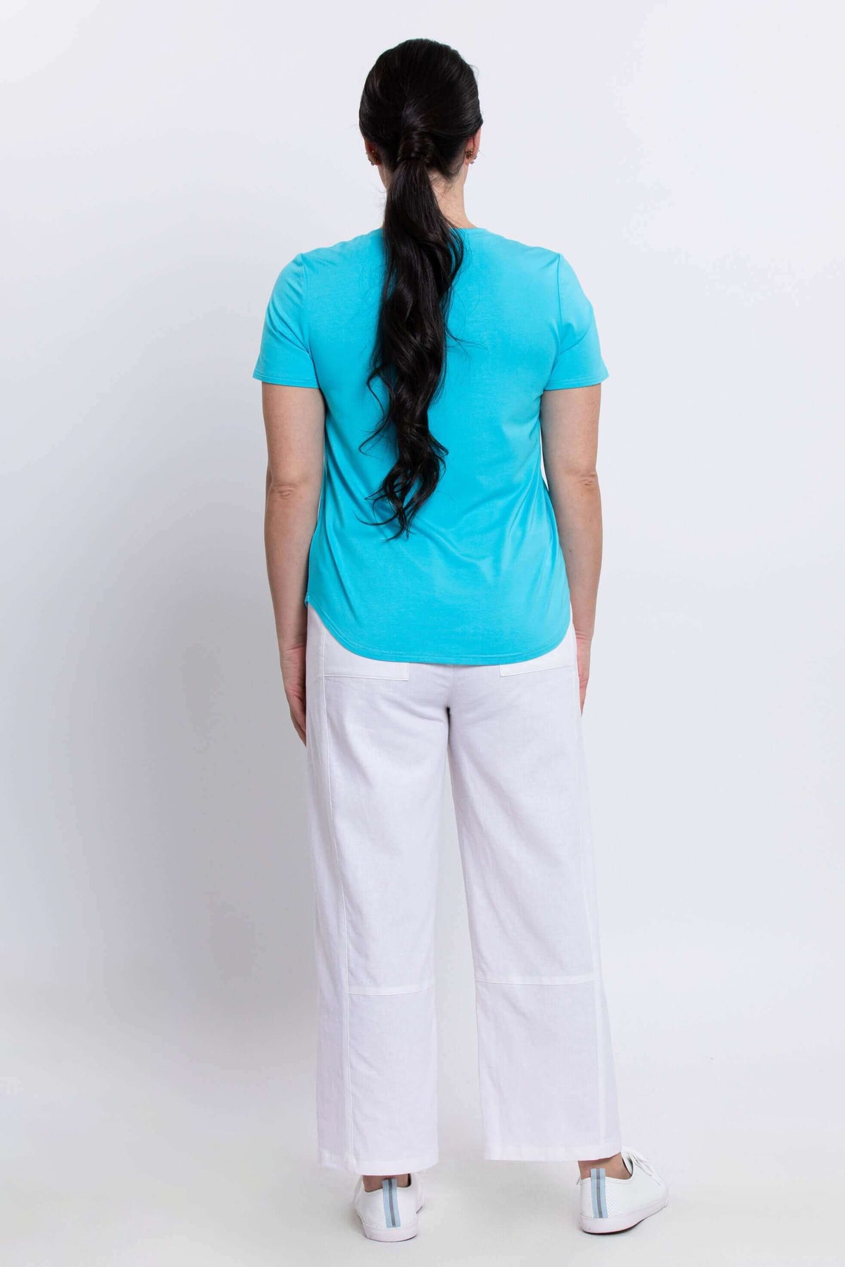 Back view of woman wearing aqua blue Tessa Tee and white pants