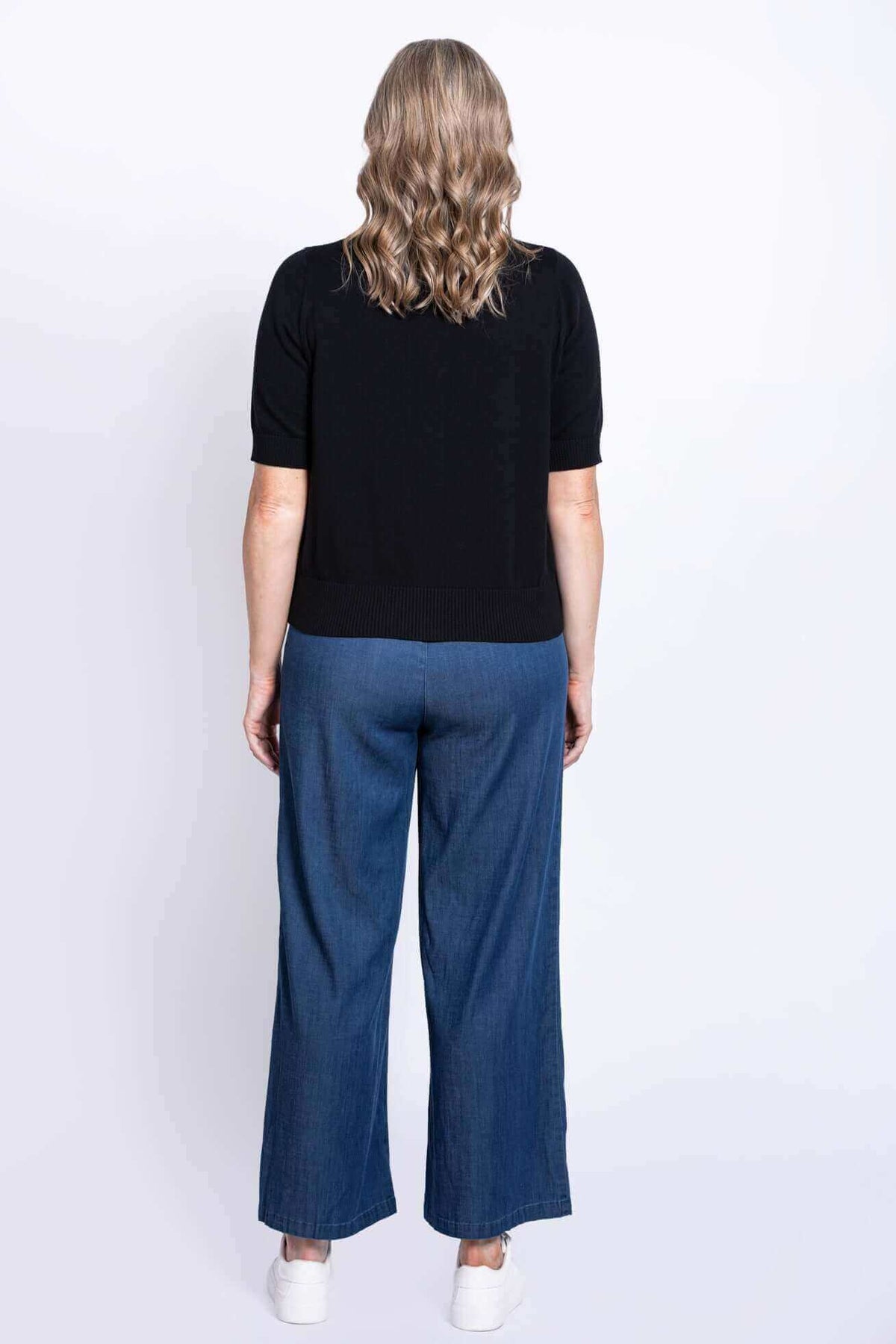 Back view of a woman in a black short-sleeve sweater and blue wide-leg pants