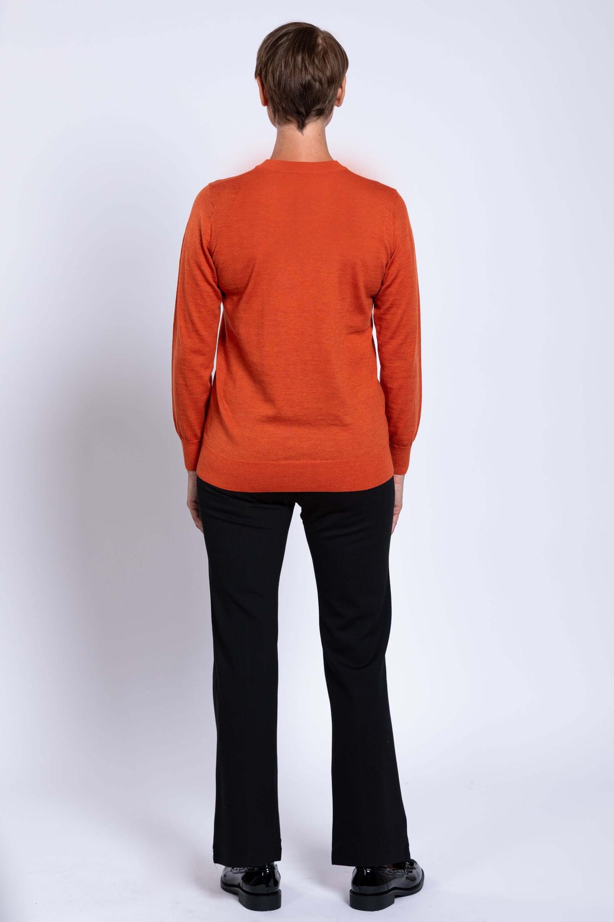 Back view of woman wearing orange V-neck sweater and black pants