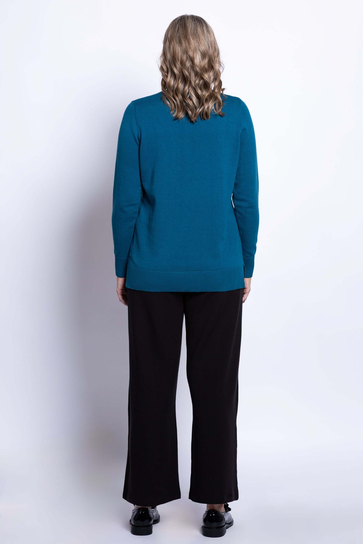 Back view of woman wearing teal V-neck cotton sweater with ribbed hem and black pants