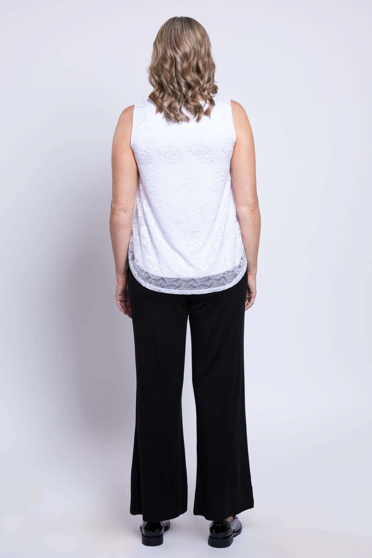 Back view of woman wearing white lace tank top and black pants
