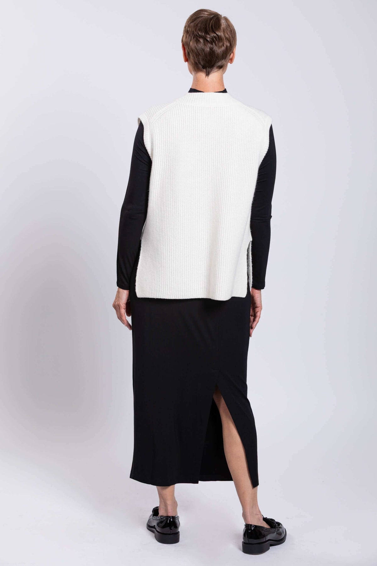 Back view of woman wearing white ribbed wool-cashmere sweater vest over black outfit